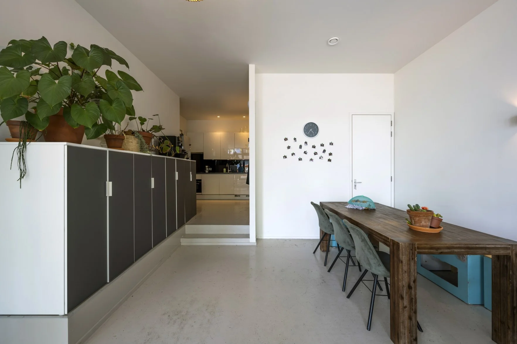 Moderne eetkamer met houten tafel, groene stoelen, kamerplanten en zicht op een open keuken aan de James Wattstraat.